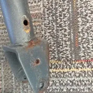 A corroded metal component with two small holes against a textured background