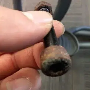 A hand holding a heavily rusted metal part, likely from fitness equipment
