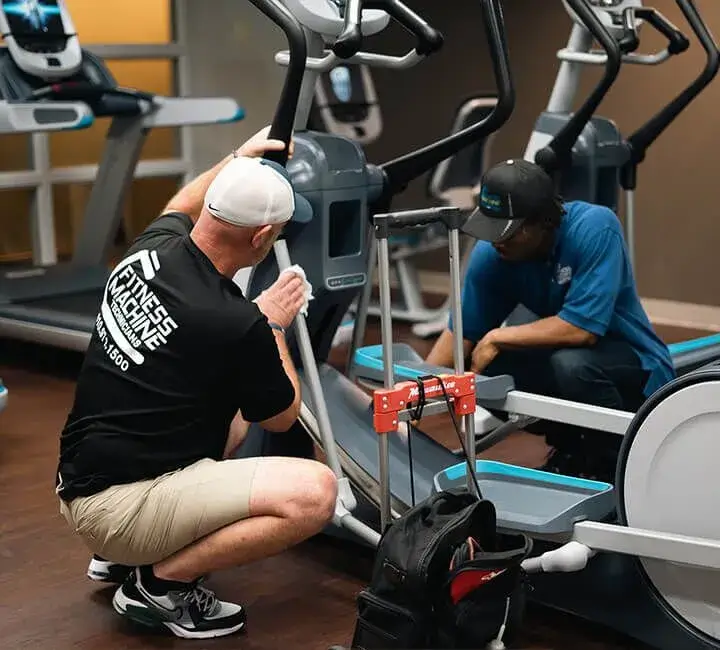 Two fitness machine technicians working on elliptical machines in a gym