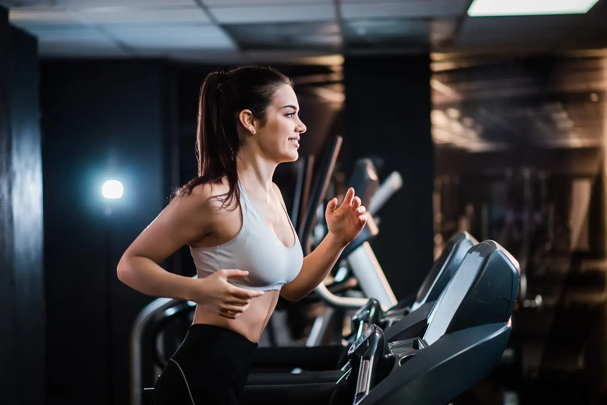 A young woman with a ponytail smiles while running on a treadmill in a gym